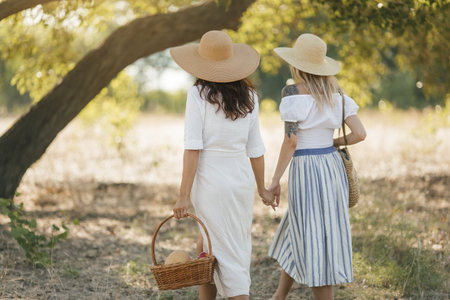 Two Stylish Women Holding Hands Walking Outdoors in Summer Lightの写真素材