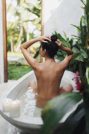Back View Of Woman In Tropical Outdoor Bath With Spa Candles And Calm Vibeの写真素材