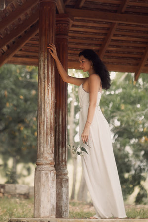 Elegant Woman in White Dress Touching Rustic Column in Outdoor Gazeboの写真素材