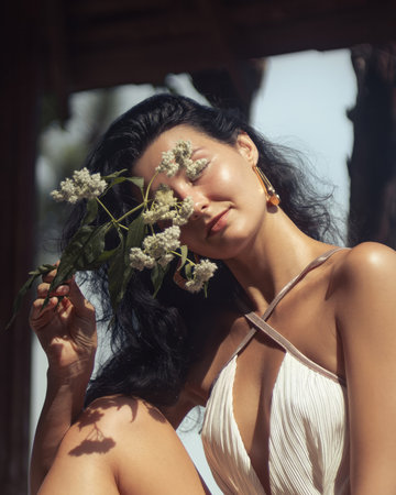 Woman in White Dress With Flowers Posing Gracefully in Natural Sunlightの写真素材