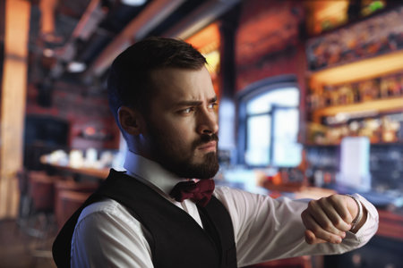 Stylish Bearded Man In Vest Checking Time At Cozy Urban Barの写真素材