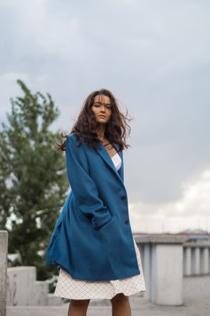 Brunette Woman in Blue Fashion Coat Standing Confidently in Urban Sceneの写真素材