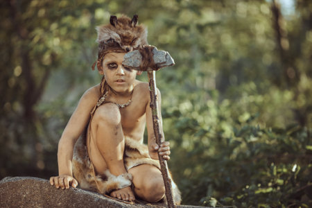 Young Primitive Boy In Fur Clothing Holding Stone Axe In Forest