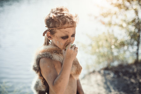 Tribal Boy Eating Fruit By Lakeside In Natural Sunlightの写真素材