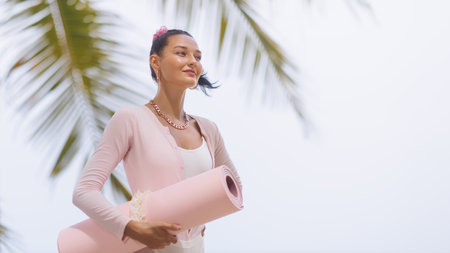 Woman in Pink Activewear Holding Yoga Mat on Sunny Tropical Beachの写真素材