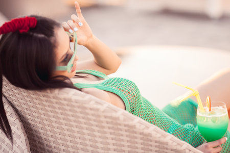 Relaxed Asian Woman in Green Mesh Dress Sunbathing With Tropical Drinkの写真素材