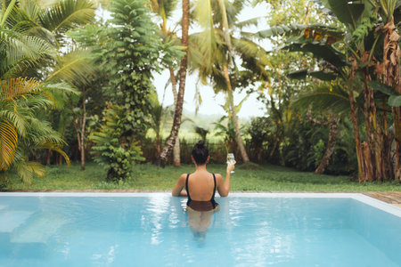 Woman Relaxing In Tropical Pool Holding Wine Glass On Luxury Vacation