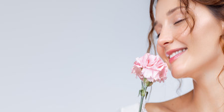 Joyful Woman Smelling Pink Carnation With Radiant Skin and Smileの写真素材