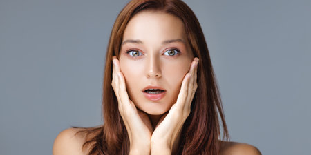 Surprised Woman With Flawless Skin Holding Face In Skincare Conceptの写真素材