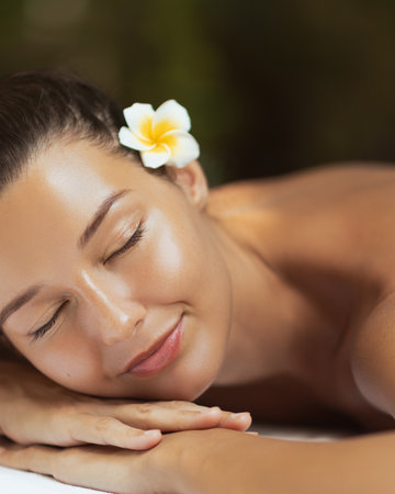 Beautiful Woman Resting on Spa Table with Glowing Skin and Tropical Flowerの写真素材