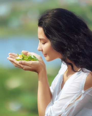 Woman in White Dress Smelling Fresh Tea Leaves and Flower Outdoorsの写真素材