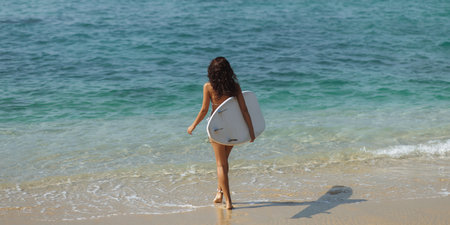 Rear View of Woman in Bikini Walking into Sea with Surfboard on Beach