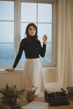 Elegant Woman Standing Thoughtfully By Window In Creative Workspace