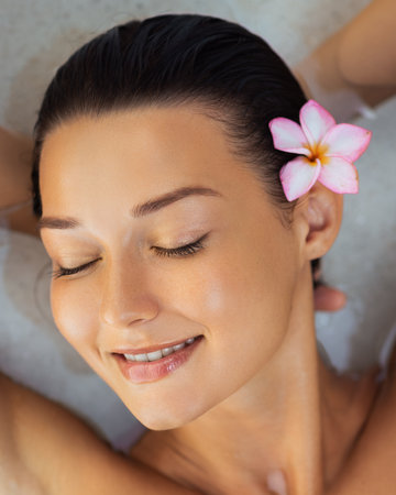 Peaceful Woman With Flower in Hair Relaxing With Hands Behind Headの写真素材