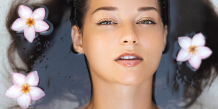 Woman Relaxing In Bathtub With Floating Flowers And Glowing Hydrated Skin