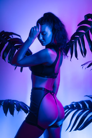 Sensual Woman in Lingerie and Neon Light Posing with Tropical Leaves