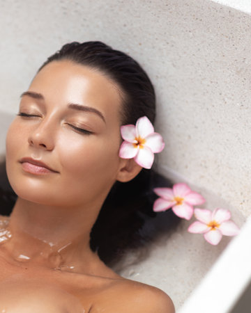 Peaceful Asian Woman Floating in Spa Bath With Frangipani and Soft Lightの写真素材