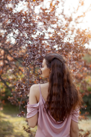 Woman in Pink Dress Walking Through Blossoming Spring Garden at Sunsetの写真素材