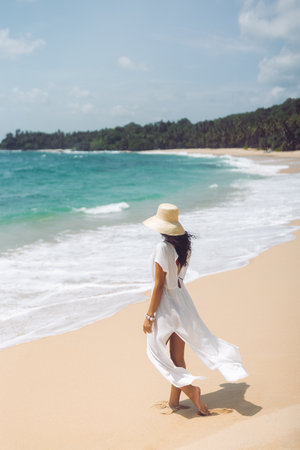 Woman in White Dress Walking Along Tropical Beach with Ocean Viewの写真素材