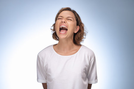 Frustrated Woman in White Shirt Screaming Loudly With Eyes Closedの写真素材