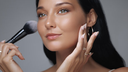 Smiling Woman Applying Makeup with Brush for Flawless and Radiant Skinの写真素材