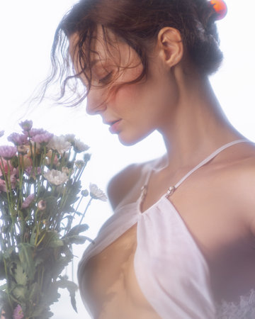 Woman in Sheer Top with Flowers in Soft Romantic Light Settingの写真素材