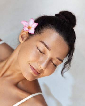 Close-Up of Asian Woman With Flower Relaxing in Spa With Eyes Closedの写真素材