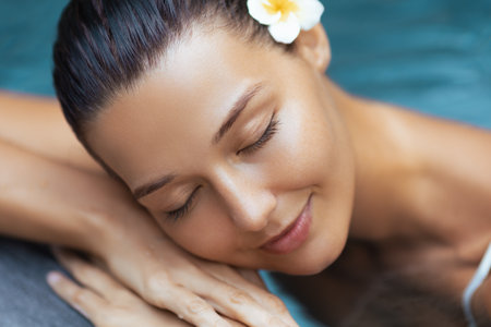 Close-Up of Asian Woman Relaxing by Pool With Frangipani and Glowing Skinの写真素材