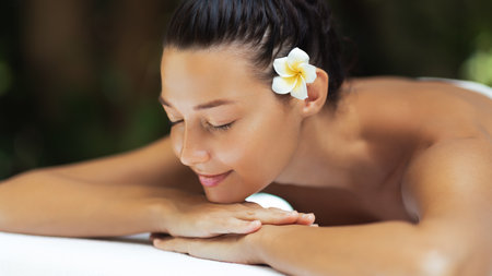 Peaceful Asian Woman Lying at Spa With Frangipani Flower and Towel Wrapの写真素材