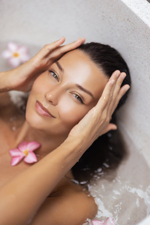 Beautiful Woman Relaxing In Spa Bath With Frangipani Flowers Wellness Conceptの写真素材