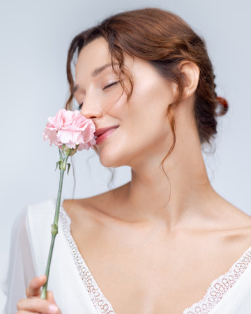Elegant Beauty Portrait Of Woman Smelling Pink Carnation In White Dressの写真素材