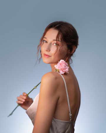 Elegant Young Woman Holding Pink Carnation Against Soft Blue Backgroundの写真素材