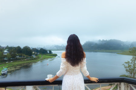 Woman Holding Tea Cup Enjoys Misty Lake View in Tea Region Sri Lankaの写真素材