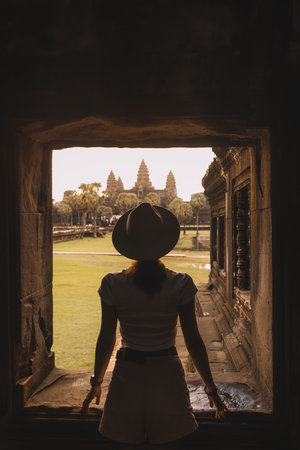 Silhouette of Female Tourist Facing Angkor Wat Through Temple Windowの写真素材