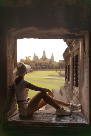 Woman Sitting Inside Temple Window Looking at Angkor Wat at Sunsetの写真素材