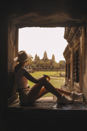 Female Tourist Sitting in Temple Window Admiring Angkor Wat Sceneryの写真素材