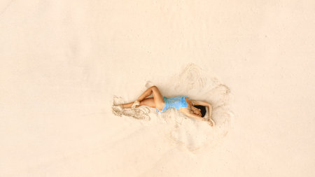 Aerial View Of Woman In Blue Dress Relaxing On Minimal Beach Sandの写真素材