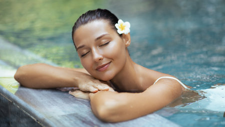 Asian Woman Relaxing in Pool With Frangipani Flower and Peaceful Expression