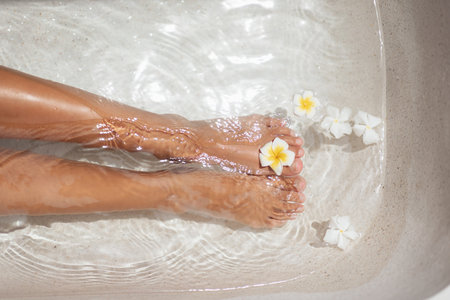 Tanned Legs in Spa Bath with Frangipani Flowers for Wellness and Skincareの写真素材
