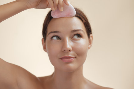 Skincare Concept With Woman Massaging Forehead Using Pink Gua Sha Toolの写真素材