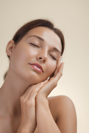 Serene Woman with Glowing Skin Touching Face Gently in Beauty Portraitの写真素材