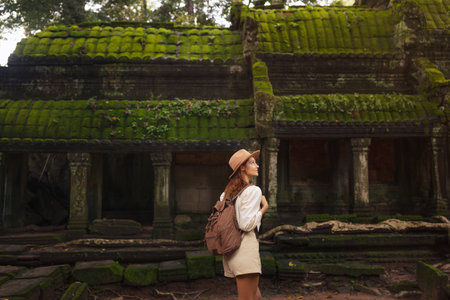 Female Traveler Admiring Moss-Covered Angkor Jungle Temple Ruins Todayの写真素材