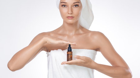 Spa Skincare Concept Woman Presenting Serum Bottle In White Towelの写真素材