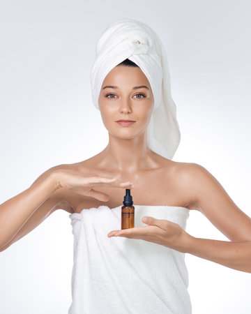 Young Woman In Towel Showcasing Skincare Oil Dropper For Ads Campaignsの写真素材