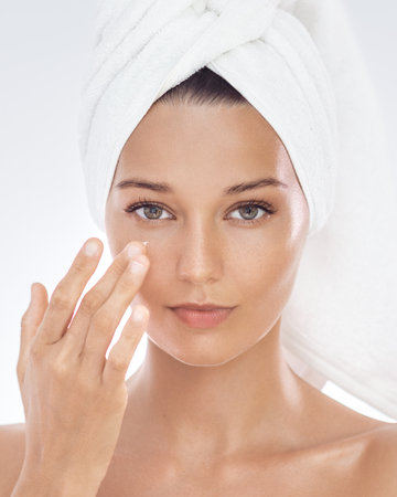 Title Smiling Woman in Towel Turban Applying Face Cream for Radiant Skinの写真素材