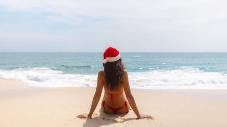 Tanned Woman in Santa Hat Relaxing in Red Bikini on Ocean Shorelineの写真素材