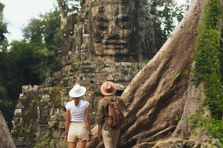 Couple Travelers Exploring Ancient Bayon Temple Stone Face Ruins In Cambodiaの写真素材