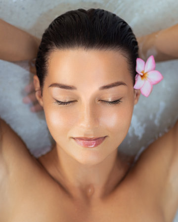 Peaceful Asian Woman Floating in Spa Water With Tropical Flower in Hairの写真素材