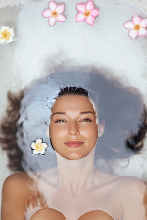 Serene Womans Face Breaking Water Surface In Spa Bath With Flowers