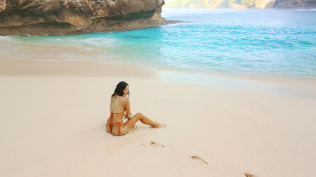 Woman Sitting On Serene Kelingking Beach With Soft Sand And Turquoise Seaの写真素材